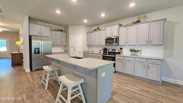 kitchen with sink, a kitchen bar, a kitchen island with sink, stainless steel appliances, and light hardwood / wood-style flooring