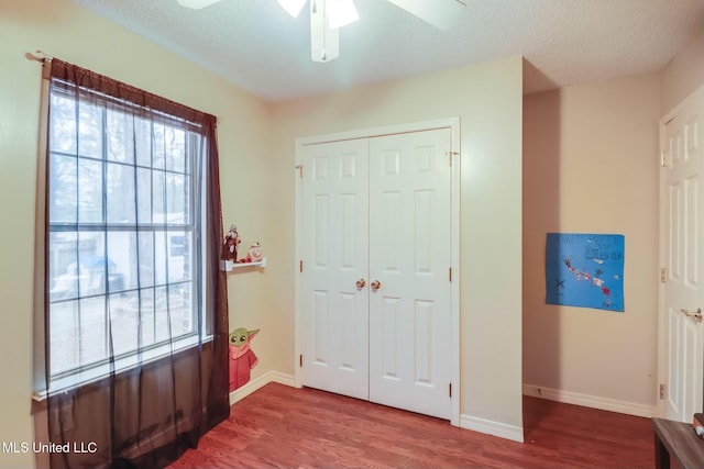 bedroom with wood finished floors, baseboards, ceiling fan, a closet, and a textured ceiling