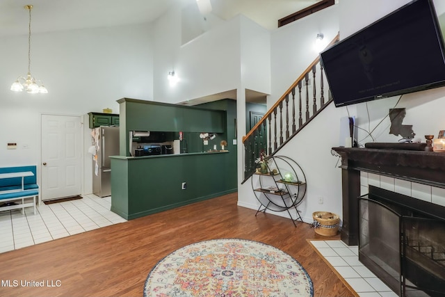 living room featuring stairway, wood finished floors, a fireplace, a towering ceiling, and a notable chandelier