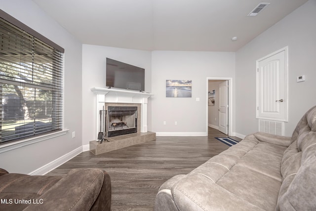 living room featuring a tiled fireplace, visible vents, baseboards, and wood finished floors