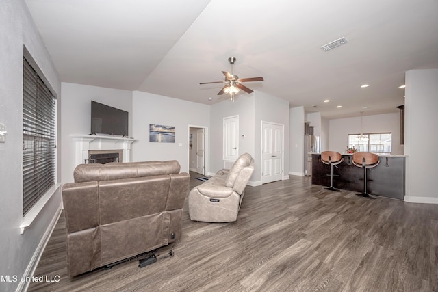 living room with visible vents, dark wood-type flooring, baseboards, ceiling fan, and a fireplace