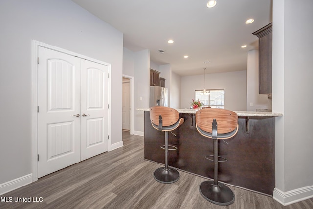 kitchen featuring baseboards, dark wood finished floors, a peninsula, stainless steel fridge with ice dispenser, and a kitchen bar