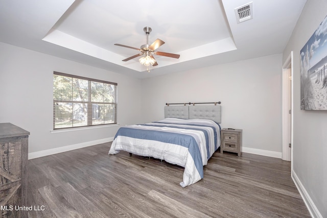 bedroom featuring visible vents, baseboards, a tray ceiling, and wood finished floors