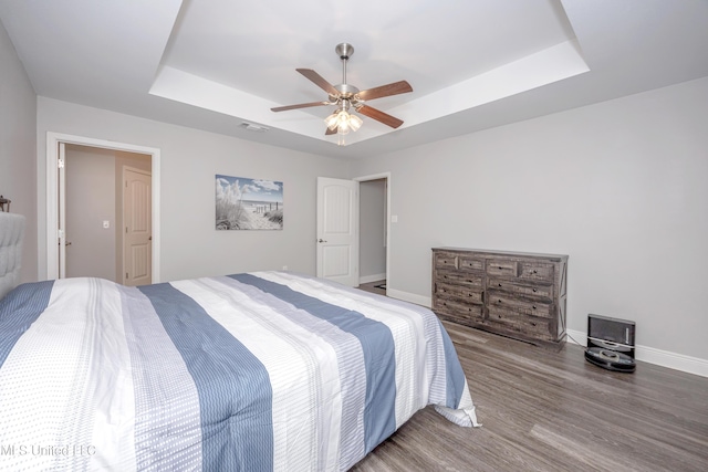 bedroom featuring visible vents, a ceiling fan, wood finished floors, baseboards, and a raised ceiling