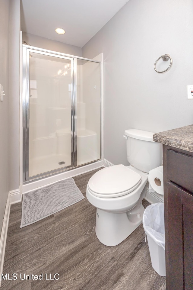 bathroom with a shower stall, toilet, vanity, and wood finished floors