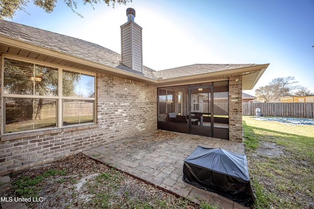 rear view of house with fence, a sunroom, a chimney, a patio area, and brick siding