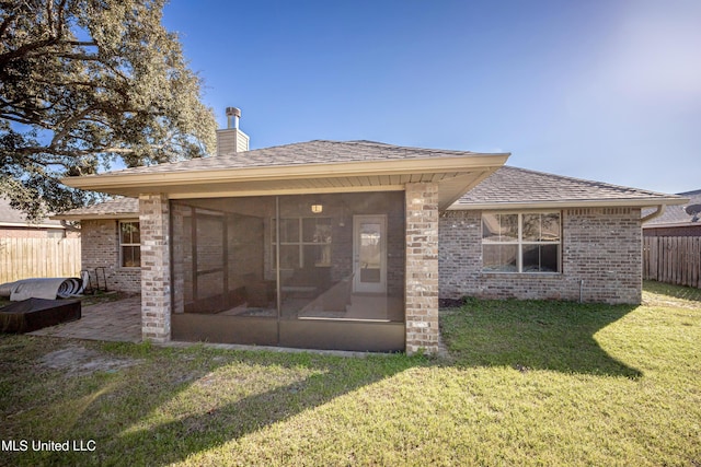 back of house featuring a yard, a sunroom, brick siding, and fence