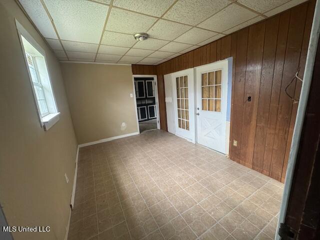 unfurnished room featuring a paneled ceiling, wood walls, tile patterned floors, and french doors