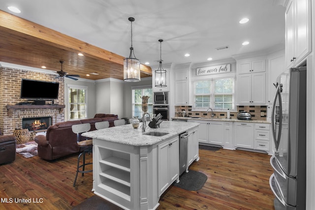 kitchen featuring an island with sink, hanging light fixtures, light stone countertops, white cabinets, and appliances with stainless steel finishes