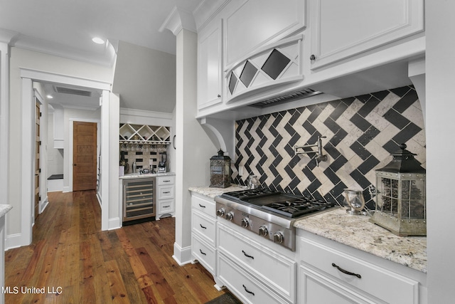 kitchen with decorative backsplash, dark wood-type flooring, beverage cooler, stainless steel gas stovetop, and white cabinetry