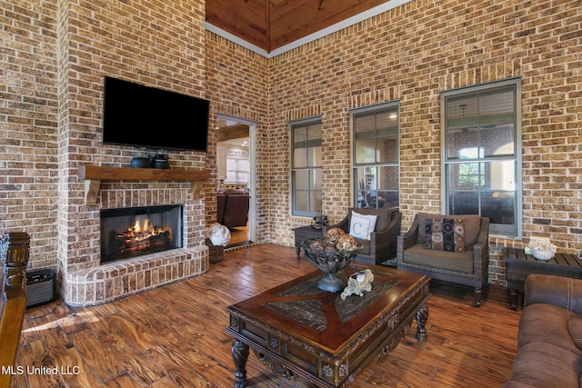 living room featuring hardwood / wood-style flooring, a high ceiling, a brick fireplace, and brick wall