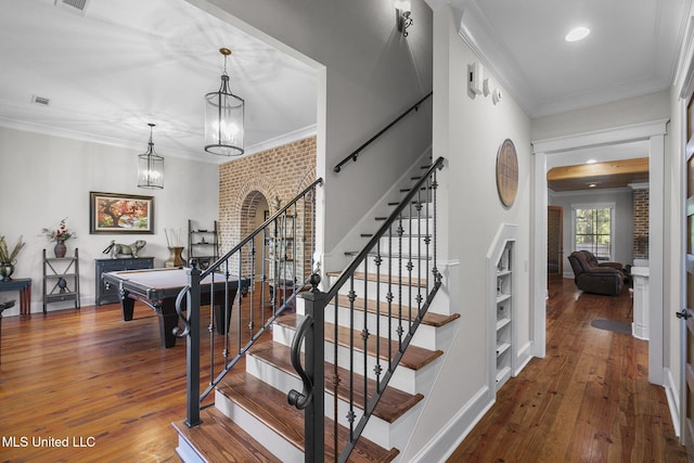 stairway featuring pool table, crown molding, hardwood / wood-style flooring, an inviting chandelier, and brick wall