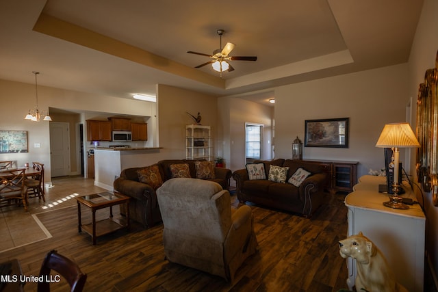 living room with ceiling fan with notable chandelier, dark hardwood / wood-style flooring, and a raised ceiling