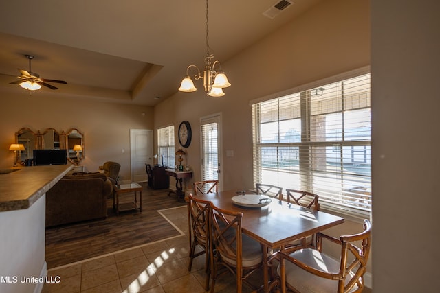 dining space featuring a tray ceiling, a wealth of natural light, dark hardwood / wood-style flooring, and ceiling fan with notable chandelier