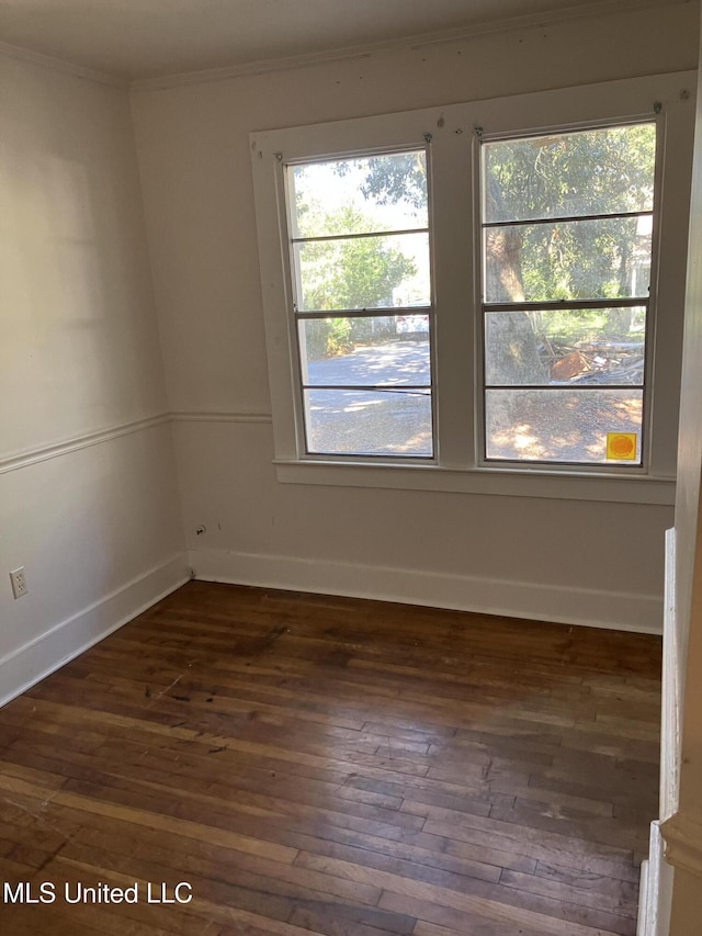 empty room with dark wood-style flooring, crown molding, and baseboards