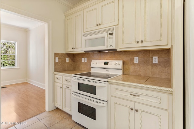 kitchen featuring cream cabinetry, backsplash, crown molding, light tile patterned floors, and white appliances