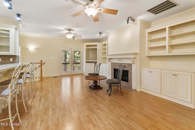 living room featuring light wood-type flooring, french doors, a tile fireplace, ceiling fan, and ornamental molding