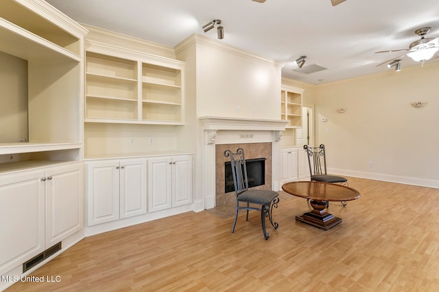 living room with ornamental molding, a tile fireplace, light wood-type flooring, and ceiling fan