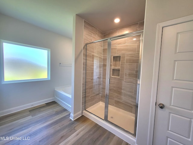 full bath featuring baseboards, wood finished floors, a stall shower, and a bath