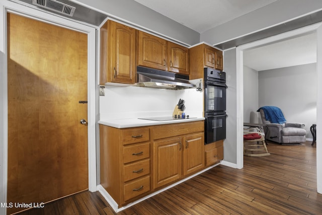 kitchen with dark wood-style flooring, light countertops, under cabinet range hood, visible vents, and black appliances