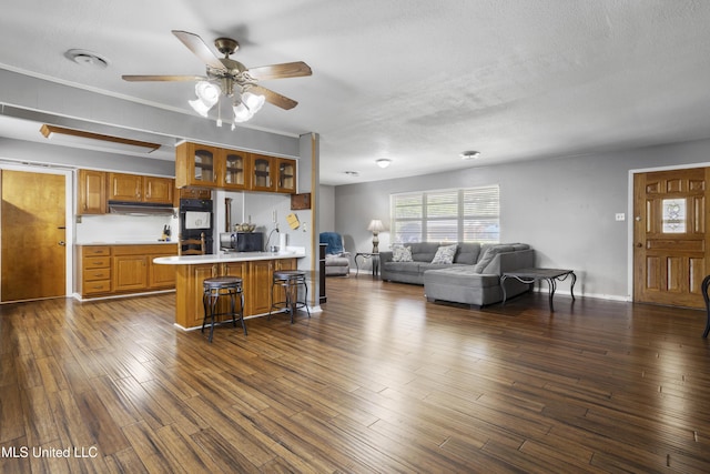 kitchen with a breakfast bar, light countertops, dobule oven black, under cabinet range hood, and glass insert cabinets
