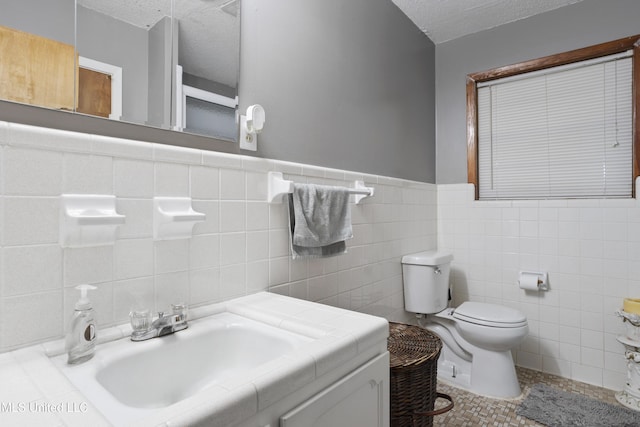 bathroom featuring a textured ceiling, tile walls, a wainscoted wall, vanity, and toilet