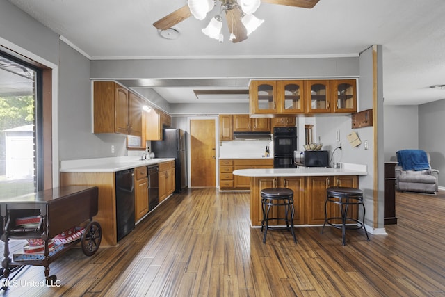 kitchen featuring a ceiling fan, black appliances, a peninsula, glass insert cabinets, and dark wood-type flooring