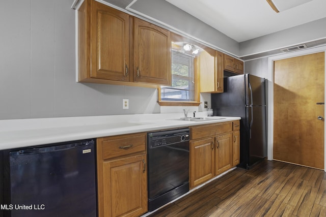 kitchen with a sink, light countertops, dark wood finished floors, visible vents, and black appliances