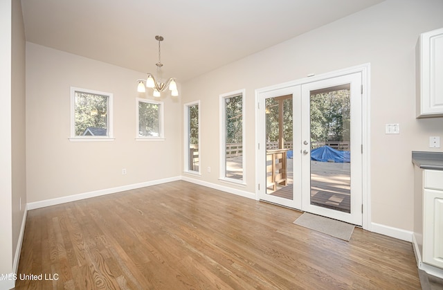 unfurnished dining area with french doors, a healthy amount of sunlight, a notable chandelier, and light wood-type flooring