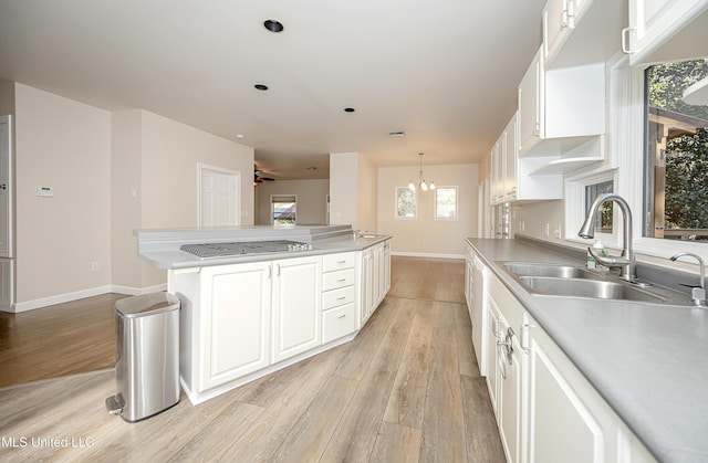 kitchen with hanging light fixtures, sink, light hardwood / wood-style flooring, white cabinetry, and stainless steel gas cooktop