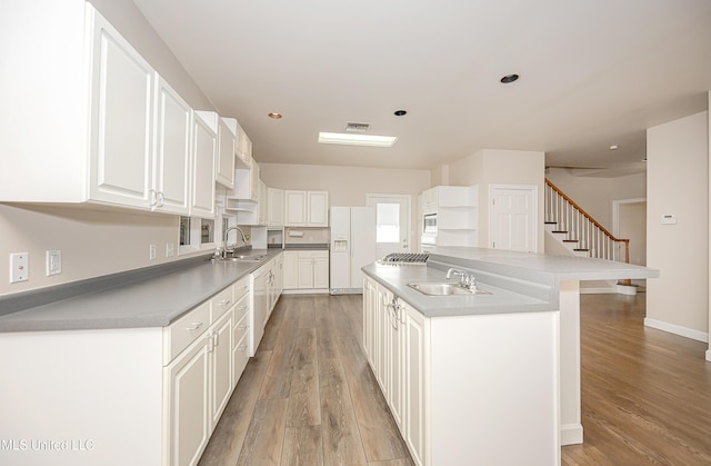 kitchen featuring sink, white fridge with ice dispenser, a kitchen island, white cabinets, and light wood-type flooring