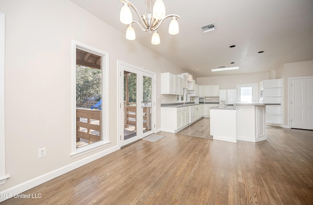 kitchen featuring pendant lighting, an inviting chandelier, white cabinets, a center island with sink, and light hardwood / wood-style floors