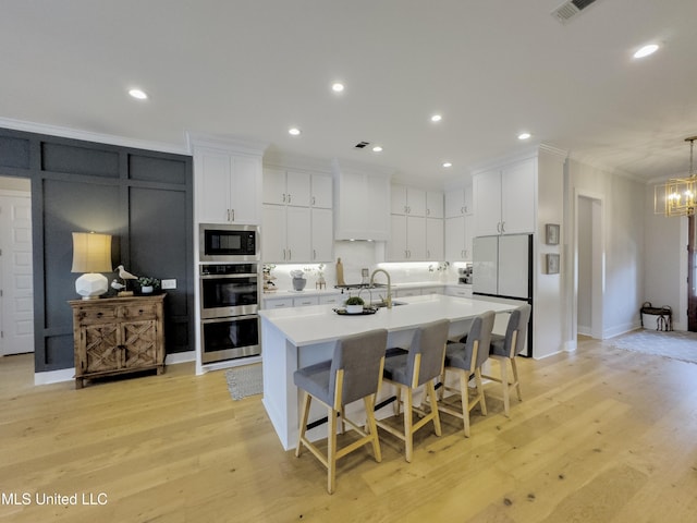 kitchen featuring white cabinets, ornamental molding, built in microwave, light countertops, and double oven