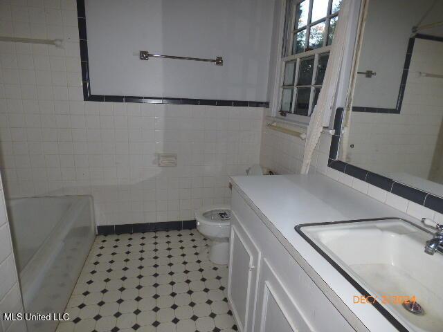 bathroom featuring tile walls, a washtub, vanity, and toilet