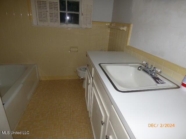 bathroom with tile walls, a bathtub, vanity, and toilet