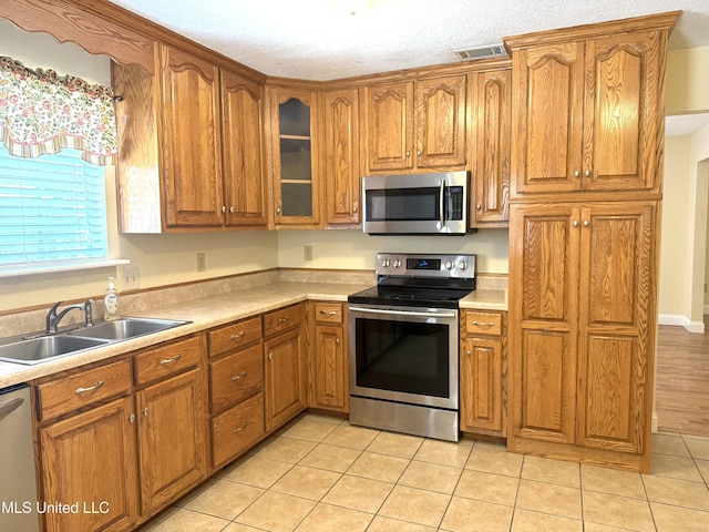 1606 Woodhaven St, Pascagoula, MS 39581 - kitchen with appliances with stainless steel finishes, a sink, brown cabinetry, light tile patterned flooring, and light countertops
