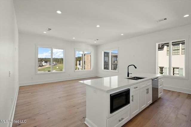 kitchen with white cabinets, sink, an island with sink, light hardwood / wood-style floors, and black microwave