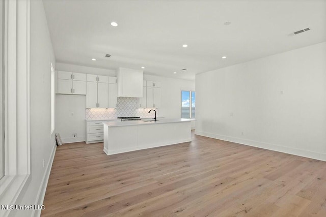 kitchen featuring a center island with sink, sink, tasteful backsplash, light hardwood / wood-style floors, and white cabinetry