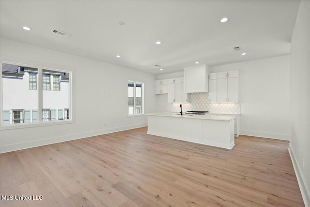 kitchen featuring a kitchen island with sink, sink, decorative backsplash, light hardwood / wood-style floors, and white cabinetry