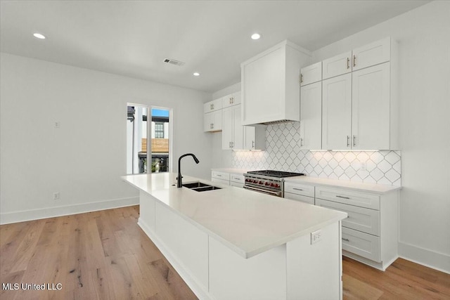 kitchen with high end stainless steel range, light hardwood / wood-style flooring, a center island with sink, and sink