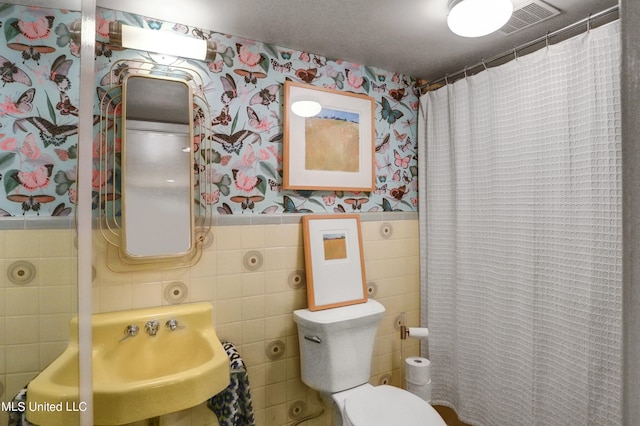 bathroom featuring tile walls, sink, curtained shower, and toilet