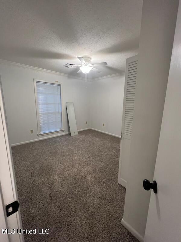 unfurnished room featuring ceiling fan, crown molding, a textured ceiling, and dark colored carpet