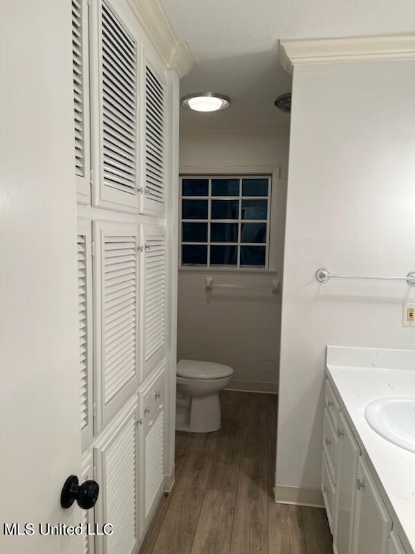 bathroom featuring toilet, vanity, hardwood / wood-style floors, ornamental molding, and tile walls