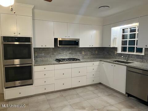 kitchen featuring light stone countertops, sink, backsplash, white cabinetry, and stainless steel appliances