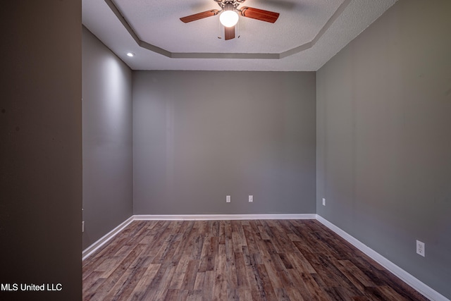 unfurnished room with a textured ceiling, wood-type flooring, ceiling fan, and a tray ceiling