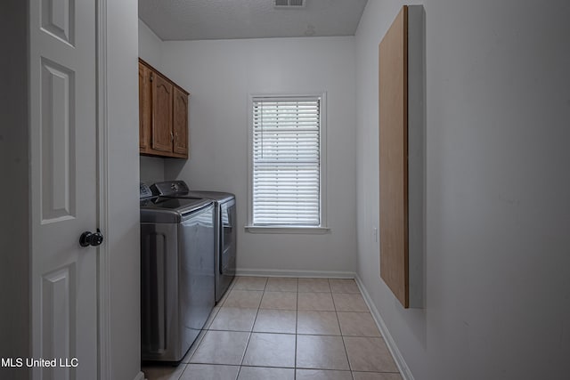 laundry area with washing machine and clothes dryer, light tile patterned flooring, cabinets, and a textured ceiling