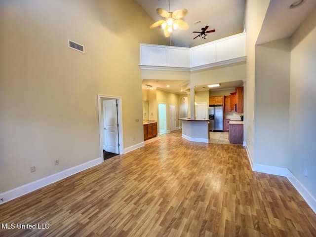 unfurnished living room with light hardwood / wood-style floors, a towering ceiling, ceiling fan, and ornate columns