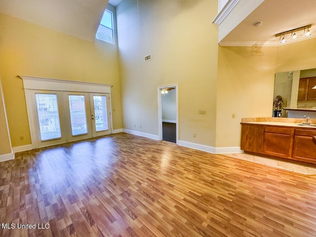 unfurnished living room featuring sink, french doors, light hardwood / wood-style flooring, and a towering ceiling