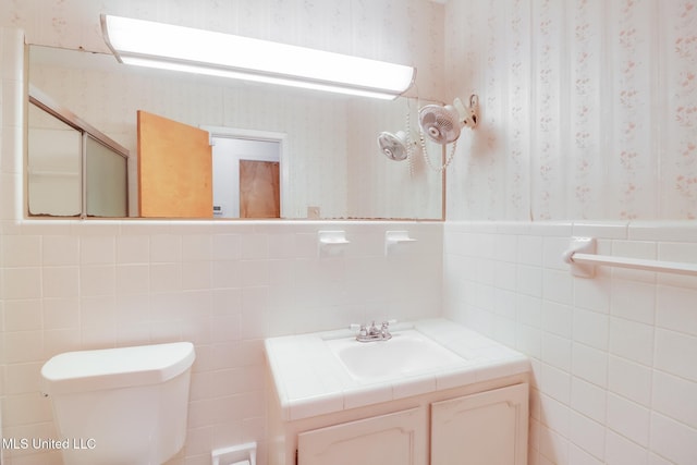 820 Lackland Dr, Biloxi, MS 39532 - bathroom with wallpapered walls, toilet, vanity, tile walls, and a wainscoted wall