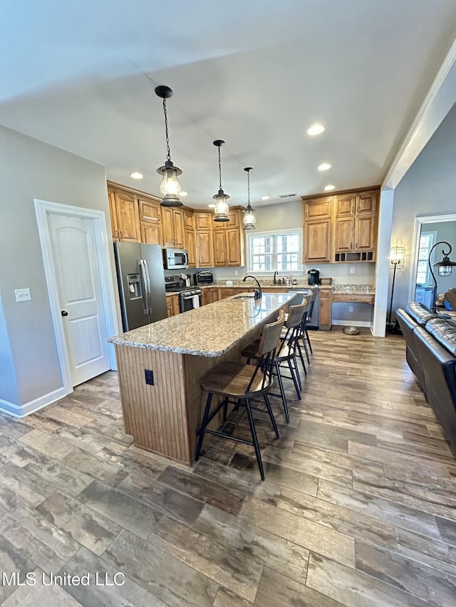 kitchen featuring a breakfast bar, hanging light fixtures, a kitchen island with sink, light stone counters, and stainless steel appliances